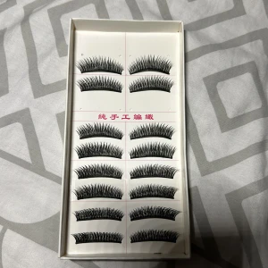 Svarta lösögonfransar i set - Ett set med 10 par svarta lösögonfransar i klassisk bågform. Fransarna är täta och ger en dramatisk look, perfekta för att framhäva ögonen. De kommer i en vit ask med rosa text och är tillverkade av syntetiskt material.