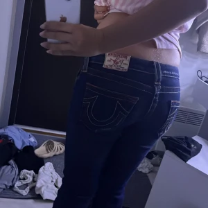 Mörkblå True Religion jeans bootcut - Säljer ett par mörkblå jeans från True Religion med ikoniska kontrastsömmar och stora bakfickor med logga. Byxorna har låg midja, bootcut-ben och detaljerade fickor med knappar. Klassisk jeanslook med snygg passform. #stockholmstil #truereligion #lowrise 