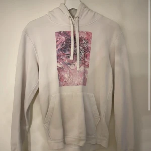 Ljus hoodie med rosa konsttryck - Säljer en ljus hoodie med snyggt rosa konsttryck framtill. Tröjan har huva med snörning och en stor magficka.