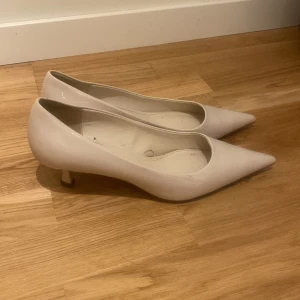 Beiga pumps med spetsig tå - Snygga pumps i beige med glansig finish och spetsig tå. Skorna har låg klack och en klassisk, elegant form som passar till många olika outfits. Perfekta för dig som gillar stilrena och tidlösa skor.
