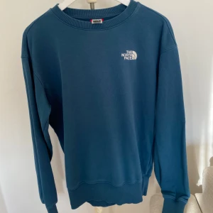 Blå sweatshirt från The North Face - Säljer en blå sweatshirt från The North Face med rund halsringning och logga på både bröstet och ryggen. Skytsnygg passform, sitter snyggt något oversized på mig som vanligtvis har S/M!