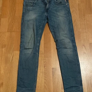 Replay Anbass jeans blå, stl 30 - Snygga blå Replay Anbass jeans i klassisk denim med lätt slitning och raka ben. Jeansen har defekt precis vid gylfen som inte syns på håll och lätt kan lagas med ett par stygn (ses på bild). Pris kan självklart även diskuteras