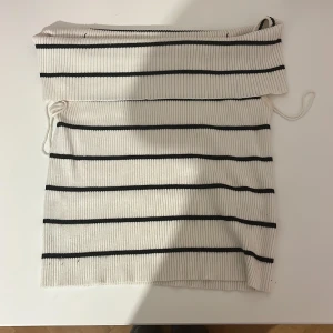 Randig offshoulder topp Vero Moda - Säljer en vit ribbad offshoulder topp från Vero Moda i storlek M. Toppen har svarta horisontella ränder och är tillverkad i mjukt, stretchigt material. Snygg croppad passform med snörning på sidan för extra detalj. Perfekt för dig som gillar stilrena och trendiga plagg.