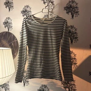 Randig långärmad tröja i bomull - Säljer en klassisk långärmad tröja från H&M i storlek S. Tröjan är vit med svarta horisontella ränder och har en rund halsringning. Tillverkad i mjuk bomull, perfekt för dig som gillar enkel och stilren design.