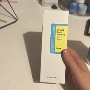 COSRX Low pH Good Morning Gel Cleanser - En mild gelrengöring från COSRX i en vit förpackning med blå och gul etikett. Innehåller 150 ml och passar perfekt för daglig rengöring av ansiktet. Låg pH-formula som rengör utan att torka ut huden.