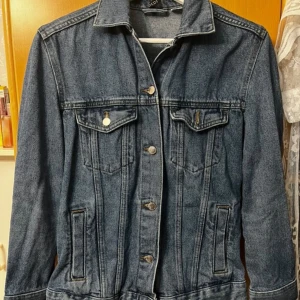 Klassisk blå jeansjacka med knappar - Snygg blå jeansjacka från Escon med klassisk passform. Jackan har två bröstfickor med lock och knappar, samt två sidofickor. Stängs med silverfärgade knappar framtill och har krage. Perfekt för dig som gillar en tidlös streetstil.