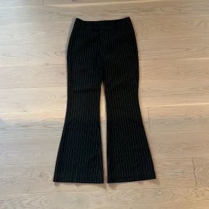 Svarta randiga bootcut kostymbyxor från Ginatricot  - Jättesnygga svarta bootcut kostymbyxor med vita tunna ränder. Byxorna är lågmidjade. De är i storlek 34. Har används ett fåtal gånger men ser knapt använda ut. 