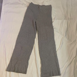 Grå ribbade stickade byxor - Mysiga grå stickade byxor med ribbad struktur och raka ben. Perfekta för chill dagar eller när du vill vara extra bekväm. Byxorna har en mjuk och stretchig känsla och är lätta att matcha med en enkel topp eller hoodie.