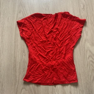 Röd topp med öppen rygg - Snygg röd topp i stretchigt material med korta ärmar och en djup öppen rygg. Perfekt för dig som vill sticka ut med en enkel men ändå cool look. Toppen har en figurnära passform och är tillverkad i mjuk bomullsmix.