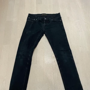 Nudie jeans - Svarta jeans från Nudie Jeans Co, modell Tight Long John. Slimmad passform med skinny ben. Extra stretch och komfort. Snygga svarta sömmar och diskret logga på bakfickan.
