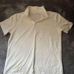 Vit frotté t-shirt från Kapahl - Vit t-shirt från Kappahl i mjuk frotté med klassisk krage och korta ärmar. Enkel och stilren design som ger en chill vibe, perfekt för varma dagar. Skön passform och lite retro känsla tack vare materialet och kragen. Skicket är 9/10 och använd fåtal gånger! 