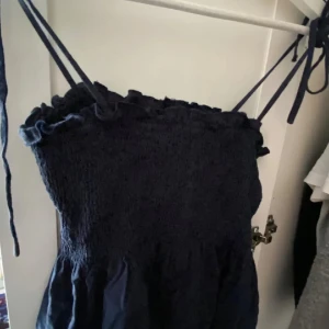 Mörkblå topp - Supersöt mörkblå topp med smockad överdel och tunna axelband som knyts. Volangdetalj upptill och luftig kjol. Perfekt för varma dagar och enkel att styla med sneakers eller sandaler.