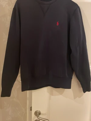 Mörkblå sweatshirt från Polo Ralph Lauren - Snygg mörkblå sweatshirt från Polo Ralph Lauren med klassisk röd broderad logga på bröstet.  Kvalité 8/10 tänker att man ska vara kring 170 lång.