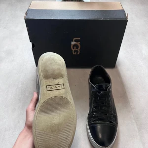 Svarta sneakers från Lanvin - Svarta sneakers från Lanvin med klassisk rund tå och snörning. Ovandel i blankt skinn och vit sula med tydlig logga undertill. Perfekta för en stilren och urban look.