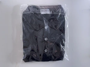 Svart skjorta från Hugo Boss - Snygg svart skjorta från Hugo Boss med klassisk krage och vita knappar framtill. Skjortan har diskret logga broderad på bröstet och är tillverkad i ett mjukt bomullstyg. Perfekt för dig som gillar stilrena och tidlösa plagg. Finns i flera storlekar, från M till L