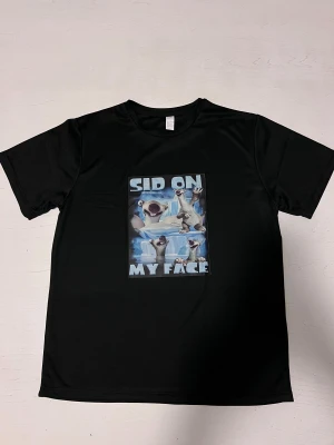 ”Sid on my face” T-shirt  - En svart t-shirt med ett humoristiskt motiv. Trycket föreställer den tecknade karaktären Sid från Ice Age med texten  “Sid on my face”. Perfekt för dig som gillar humoristiska och uppseendeväckande tryck. Tröjan är i nytt skick och sitter bekvämt.
