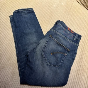 Dondup jeans  - Snygga blå jeans från Dondup, Made in Italy. Klassisk femficksmodell med raka ben och diskret slitning på framsidan för en cool look. Jeansen har orangea sömmar och metallnitar vid fickorna. Perfekt för dig som gillar italiensk design och stil.