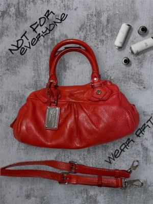 Marc Jacobs Röd Handväska  - Eftertraktade väskan från Marc Javobs Cool röd handväska från Marc Jacobs med silverfärgad metallbricka framtill. Väskan är gjord i mjukt skinn och har både handtag och avtagbar axelrem med metallspännen. Snygga detaljer och en rundad, rymlig form som sticker ut. Lite smutsig i kanter i väskan men skit bra skick annars, be om mer bilder. 100% läder från ko, cowleather