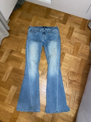 True Religion ljusblå bootcut jeans -  ljusblå low/mid rise jeans från True Religion med broderade fickor och silverfärgade knappar bak. 