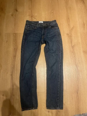 Mörkblå jeans från Jack & Jones - Snygga mörkblå jeans från Jack & Jones med klassisk femficksdesign och raka ben. Jeansen har en normal passform och är tillverkade i slitstarkt denim med kontrastsömmar och läderpatch bak i midjan. Perfekta för en chill och stilren look. 29/34