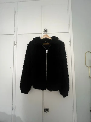 Svart teddyjacka med dragkedja - Passar mig som har storlek S. Sitter som en M skulle jag säga. Mjuk och fluffig svart teddyjacka från H&M med hel dragkedja framtill. Jackan har långärmade ärmar och ribbade muddar vid ärmslut och nederkant. Perfekt med ett par jeans till. Jackan har en loose passform.