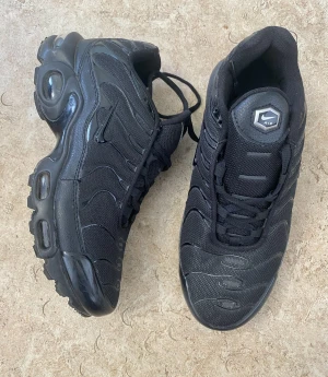 Svarta Nike Air Max sneakers - Säljer ett par helsvarta Nike Air Max sneakers med chunky sula och synliga luftbubblor. Skorna har mesh och syntetmaterial i ovandelen, diskret swoosh på sidan och snörning framtill. Perfekta för dig som gillar en sportig och clean look.