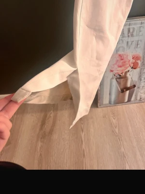 Vita raka byxor från BikBok, stl 38 - Snygga vita byxor från BikBok i rak modell med croppad längd och slits nertill. Byxorna har fickor fram, bälteshällor och stängs med dragkedja och hake. Perfekta för en clean och fräsch look. Materialet känns som bomull med lite stretch. VILL BLI SV MED DOL FORT!!