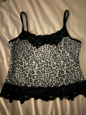Leopardmönstrad linnetopp från Romwe - Säljer en snygg leopardmönstrad linnetopp från Romwe i storlek S. Toppen har svarta spetsdetaljer vid halsringning och nederkant, tunna axelband och croppad passform. Färgen är beige med svarta leopardfläckar och svarta spetskanter. Perfekt för dig som gillar djurmönster och vill sticka ut.