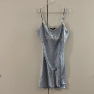 Ljusblå spetsklänning Gina Tricot - Supersöt ljusblå kort klänning från Gina Tricot med tunna axelband och vacker vit spets längs urringningen. Klänningen har en slinky satinliknande känsla och sitter figurnära. Perfekt för dig som gillar en feminin och trendig look. En liten fläck, sitter som S/M