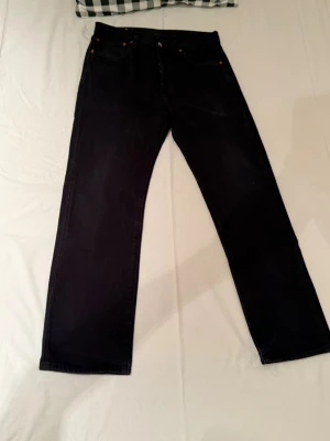 Svarta Levi's 501 jeans straight fit - Klassiska svarta Levi's 501 jeans med rak passform och fem fickor. Jeansen har knappgylf och är tillverkade i robust denim. Perfekta för dig som gillar en tidlös och clean look. Använd fåtal gånger storlek W31 L30