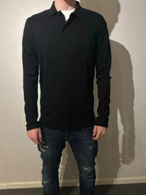 Svart långärmad polotopp Selected Homme - Svart långärmad polotopp från Selected Homme i klassisk design med krage och knappslå. Tillverkad i mjuk bomull som känns skön mot huden. Modellen är 183 