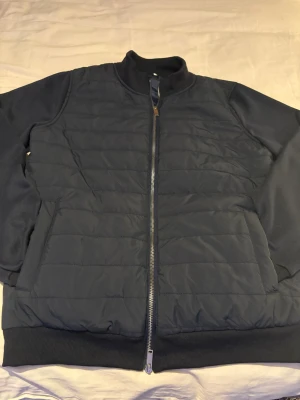 Mörkblå cardigan - Snygg mörkblå cardigan med quiltad framsida och baksida, hel dragkedja och ribbade muddar. Jackan har en stilren look och är perfekt för kyligare dagar.   Storlek M men passar stor S. Använd 2-3 gånger 