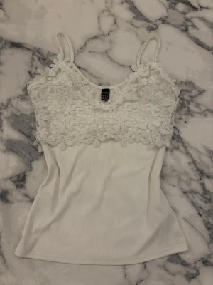 Vit linnetopp - Supersöt vit linnetopp från SHEIN i storlek XS. Toppen har smala axelband och är dekorerad med blommig spets upptill, vilket ger en romantisk vibe. Materialet är ribbad och stretchigt.