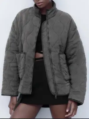 Säljer en grå quiltad jacka och hög krage. Jackan har två stora fickor framtill, dragkedja och justerbar snörning nedtill. 