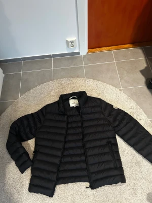 Svart jacka från moncler  - Svart dunjacka från Moncler med quiltad design och dragkedja framtill. Jackan har lång ärm, ståkrage samt Moncler-logga på vänster ärm. Insidan har den klassiska serietidningsdetaljen samt en röd dragkedja på innerfickan. Jag säljer jackan då den var för stor för mig. Jackan är i storlek 3, vilket motsvarar L. Tveka inte på att höra fig vid funderingar!