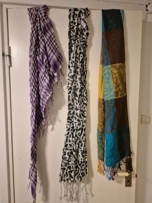 Tre snygga sjalar i olika mönster - Säljer tre sjalar: en lila och vit rutig med glittriga inslag, en vit med svart leopardmönster och glittrig finish, samt en patchwork-sjal med färger som blå, röd, gul och brun med blommigt mönster. Perfekt för att lyfta din outfit med färg och mönster.