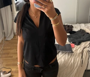 Svart v-ringad blus med kort ärm - Säljer en svart blus med v-ringning och korta ärmar. Toppen har en clean och enkel design med lätt croppad passform. Perfekt till jeans eller kjol för en stilren look. Materialet känns mjukt och följsamt, troligen polyester eller bomull.