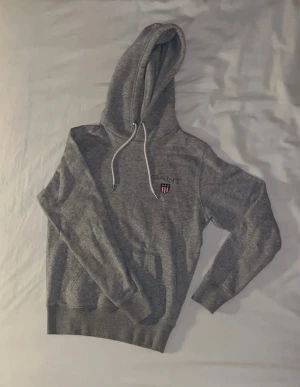 Grå Gant hoodie - Väldigt skön grå Gant hoodie. Säljer då den blivit lite för liten. Använd men i bra skick.
