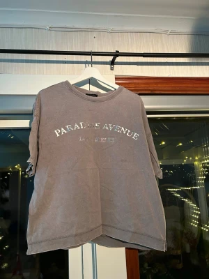 Grå t-shirt strl. M - En fin t-shirt som tyvärr blev lite använd. ”Paradise avenue” tryck med rhinestones under (alla kvar). En liten slit längst ner på båda sidorna som lägger till en fin detalj. 