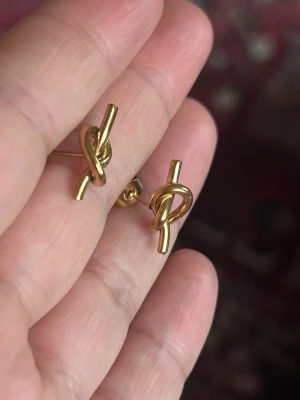 stål  guldfärgade örhängen  - Säljer  ett par stål  guldfärgade örhängen med knutdesign. 1,7 cm lång  0,6 mm bred 