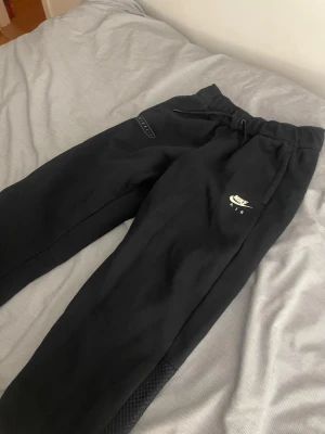Svarta Nike Air mjukisbyxor XL - Svarta mjukisbyxor från Nike Air i storlek XL, med tryckt logga på ena benet och snörning i midjan. Byxorna har en loose passform och är gjorda i mjukt bomullsmaterial, perfekta för chill eller träning. Snygga detaljer med Nike Air-tryck på båda benen.pris kan diskuteras 