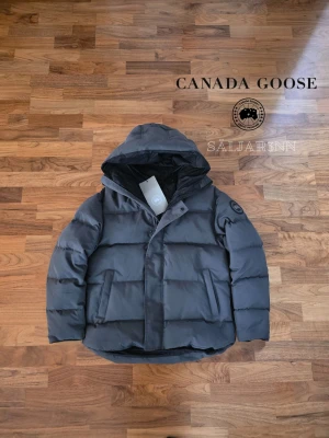 Grå Canada Goose Macmillan Parka - ⚪️ Canada Goose Macmillan Parka Black Label ⚪️ Exklusiv och mycket varm vinterjacka från Canada Goose i Black Label-utförande med svart emblem och stilren premiumdesign. Helt ny, tagg avklippt.. Perfect för nordiskt klimat med tjock dunfyllning, skyddande huva och djupa dragkedjefickor. En lyxig och praktisk vinterfavorit.  📦 Snabb leverans – skickas samma dag 📩 Skriv vid intresse