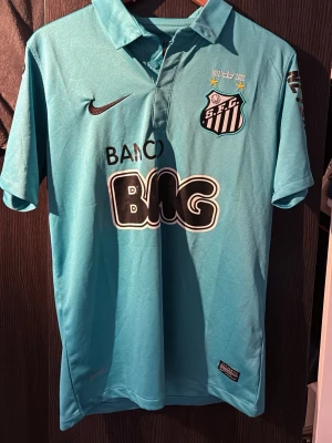 Turkos Santos FC Neymar Jr tröja Nike - Säljer en turkos Santos FC matchtröja från Nike med Neymar Jr och nummer 11 på ryggen. Tröjan har Dri-Fit material, svart tryck och klubbmärke på bröstet. Snygga sponsorloggor och klassisk krage. Perfekt för dig som älskar fotboll och vill sticka ut. Priset kan diskuteras