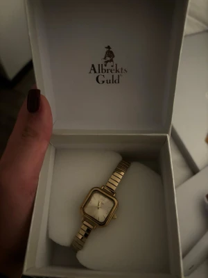 En elegant guld klocka ifrån Alberkts Guld - en guldfärgad klocka från Albrekts Guld med fyrkantig urtavla och metallarmband, men ingen väst finns med.❤️