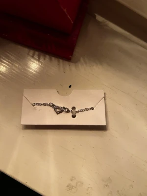 silvrigt armband med ett hjärta -  ett armband  i silverfärgad metall med ett hjärtformat hänge.