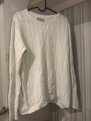 Vit kabelstickad tröja Basic You - Säljer en vit kabelstickad tröja från Basic You i ekologisk bomull. Tröjan har rund hals, ribbade muddar och långärmad design. Perfekt för dig som gillar klassisk stil med twist. Passar till jeans eller kjol och är supermjuk mot huden.