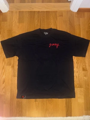 Svart t-shirt från Sway med röd text - Svart t-shirt från Sway med röd 'sway'-logga tryckt på bröstet och i nacken. Klassisk rund hals och korta ärmar. Tillverkad i mjuk bomull som känns skön mot huden. Perfekt för dig som gillar enkel och stilren streetwear.
