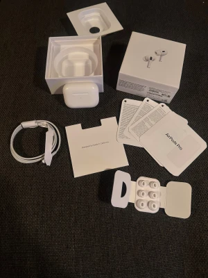 AirPods Pro (2nd generation) - Apple AirPods Pro (2nd gen) med originalförpackning, laddningskabel, extra öronkuddar och manualer. Produkten ser ut att vara i mycket gott skick utan synligt slitage. Aktiv brusreducering och MagSafe-laddning ingår. Perfekt för trådlös musik och samtal.