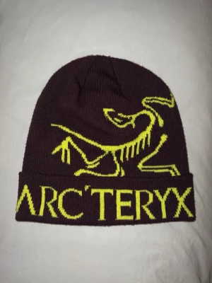 Brun mössa från Arc'teryx - Säljer en brun mössa från Arc'teryx med gul logga och text framtill. Använd men har fortfarande mycket liv kvar. Skriv vid funderingar eller fler bilder!