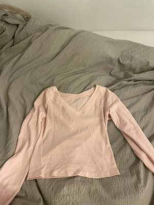 Ljusrosa långärmad topp med v-ringning - Säljer en ljusrosa långärmad topp med v-ringning. Toppen är croppad och har en enkel, stilren design utan mönster eller extra detaljer. Perfekt att matcha med jeans eller kjol för en chill look.
